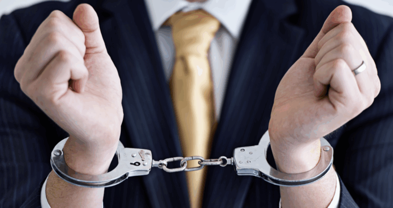 Close up of man's wrists in handcuffs, wearing a blue suit jacket and yellow tie | Daniel Stark Law